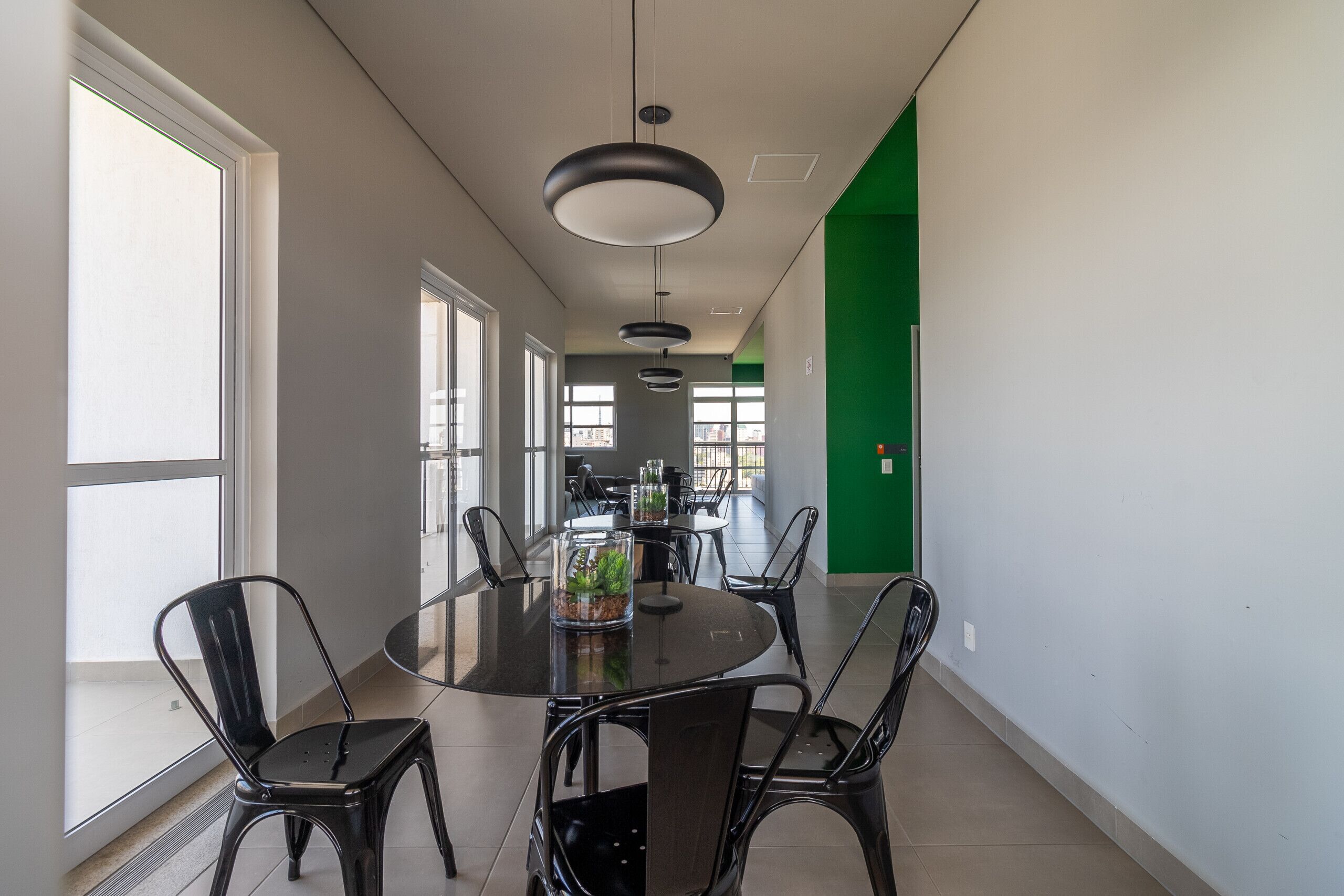 A modern dining area with a round table, black chairs, pendant lights, and a view of a cityscape through large windows.