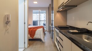 A narrow hotel corridor with a bed, kitchenette, and a view of a balcony. - Ycp704 in S o Paulo (São Paulo)
