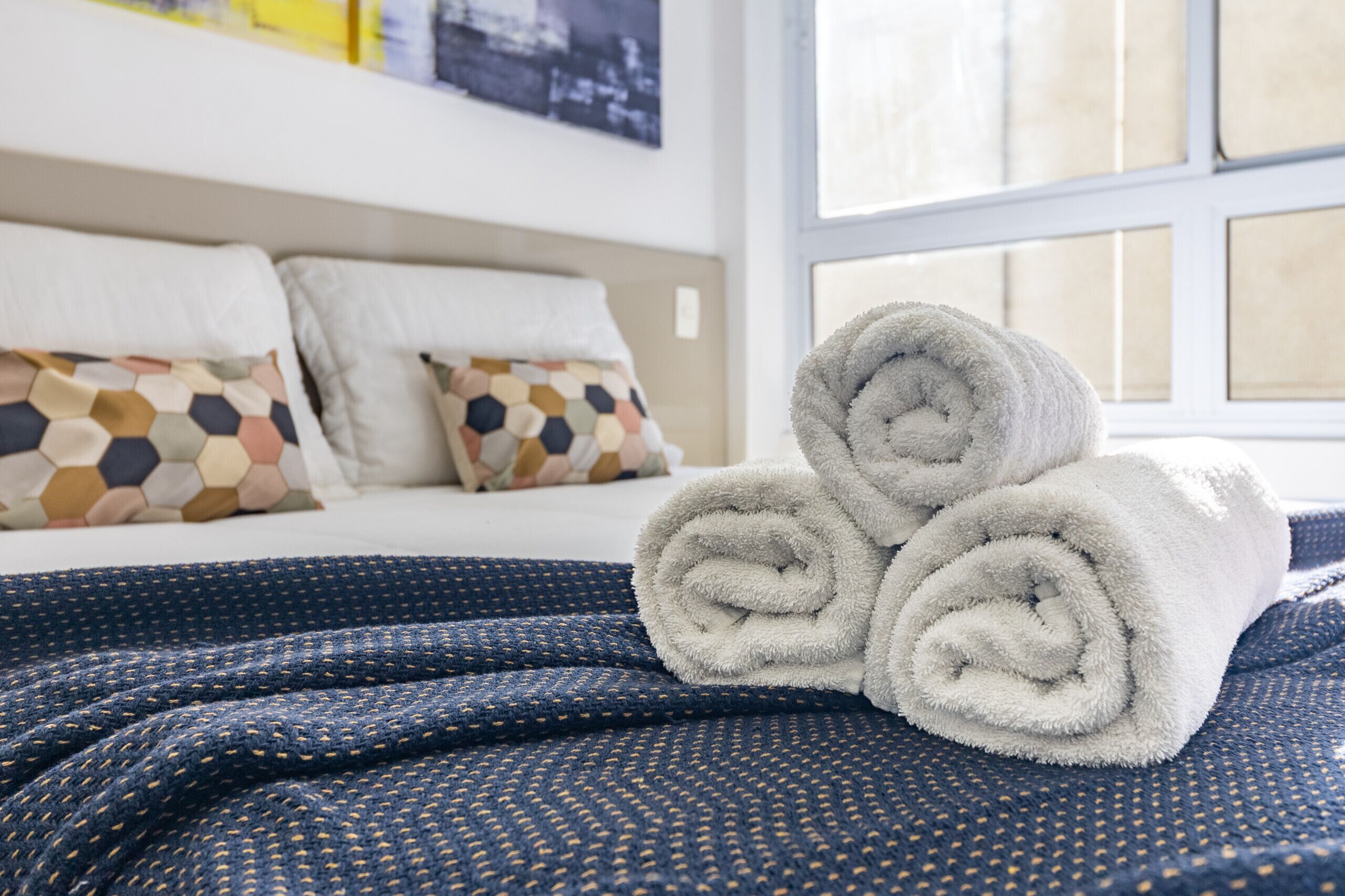 A neatly made bed with rolled white towels, a patterned blue blanket, and hexagonal pillows.