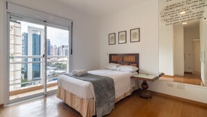 A hotel room with a bed, a bedside table, a large window with a city view, and a wall with framed artwork. - Ia71 Apto 3 Quartos Itaim 4p 3q (São Paulo)