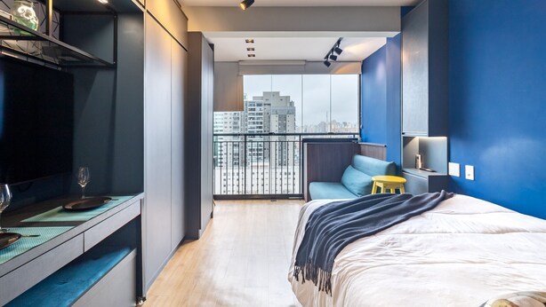 A modern bedroom with a large bed, a desk with a chair, a small stool, and a TV. - Ycp2206 in S o Paulo (São Paulo)