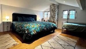 Un dormitorio con una cama grande, una cama más pequeña, una mesita de noche, una lámpara, un ventanal y vistas al exterior.