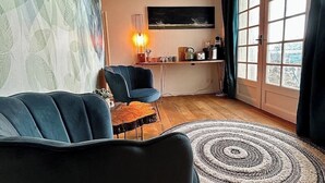 Un salón con sofá, una silla, una mesa de centro, una lámpara, un cuadro y vistas al exterior por una ventana.