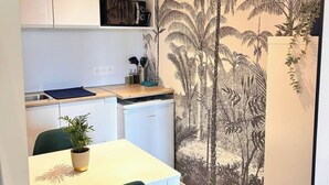 Una cocina compacta con armarios blancos, una pequeña encimera y un lavavajillas. Hay una planta en maceta sobre la mesa y un mural de palmeras en la pared.