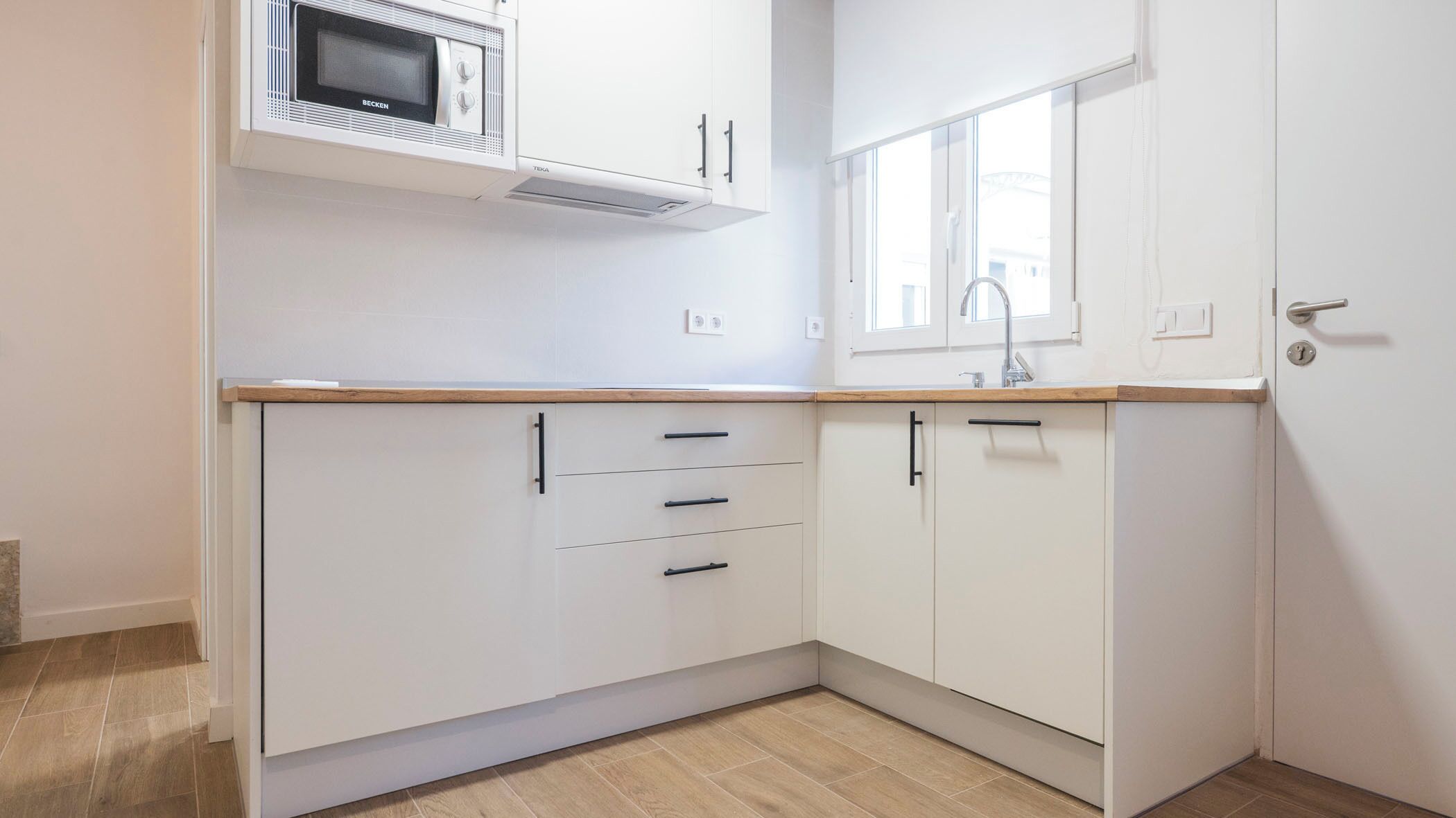 Una cocina con armarios blancos, un microondas y una ventana sobre el fregadero.