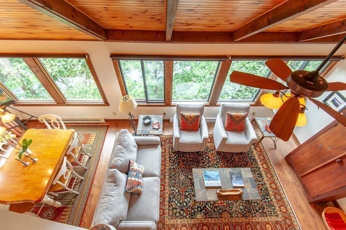 Un'ampia zona giorno con soffitto alto, grandi finestre, una ventola a soffitto e un tavolo da pranzo con sedie.