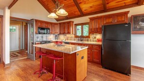 A kitchen with wooden cabinets, a black refrigerator, a granite countertop, and a red bar stool.