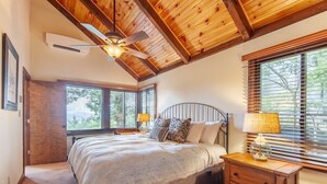 A bedroom with a large bed, a ceiling fan, a nightstand with a lamp, and a window with blinds.