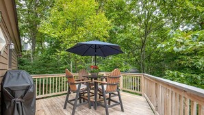 A wooden deck with a table and chairs, a grill, and an umbrella.