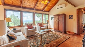 A spacious living room with a high wooden ceiling, large windows, and a view of the outdoors.