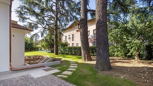 A stone pathway leading to a building with a tiled roof, surrounded by trees and a grassy area. - NEW Green Apartments & Parking. Magnolia Apartment. Vimercate-Monza (Vimercate)