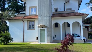 A modern two-story house with a stone facade, a tiled roof, and a well-maintained lawn. - NEW Green Apartments & Parking. Magnolia Apartment. Vimercate-Monza (Vimercate)