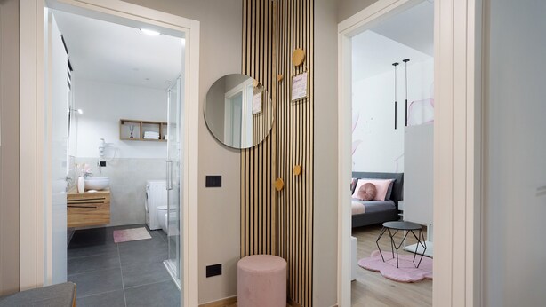 A modern bathroom with a glass shower, a round mirror, and a wooden vanity. - NEW Green Apartments & Parking. Magnolia Apartment. Vimercate-Monza (Vimercate)