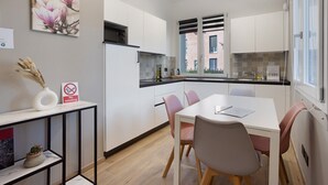 A modern kitchen with white cabinets, a black countertop, and a dining area with a white table and pink chairs. - NEW Green Apartments & Parking. Magnolia Apartment. Vimercate-Monza (Vimercate)