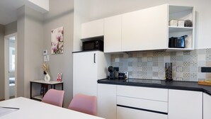 A modern kitchen with white cabinets, a black countertop, and a microwave. There is a dining table with chairs, a vase with dried flowers, and a picture of flowers on the wall. - NEW Green Apartments & Parking. Magnolia Apartment. Vimercate-Monza (Vimercate)
