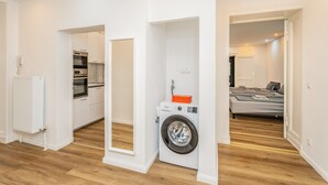 Un appartement moderne comprenant un espace buanderie, une kitchenette et une chambre avec un lit et un canapé.