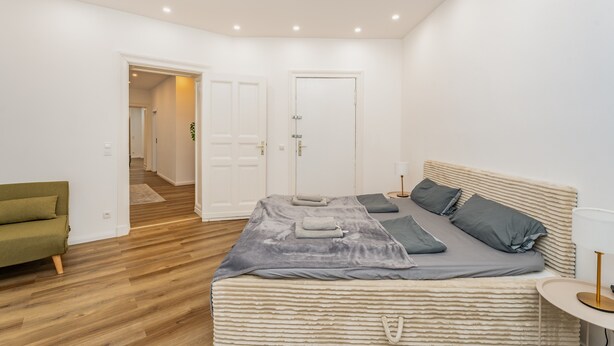 Une chambre à coucher avec un lit, un canapé vert, une table de chevet et une porte donnant sur une autre pièce.