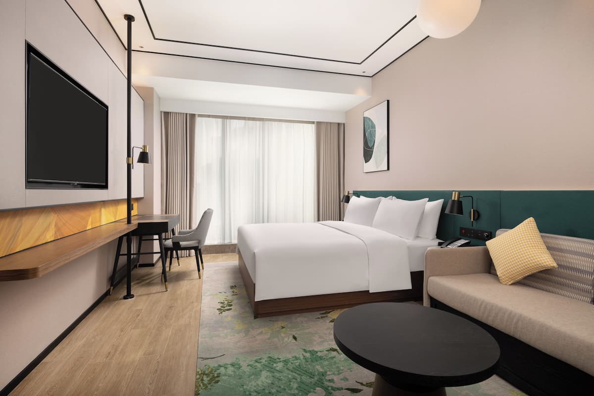 Ein modernes Hotelzimmer mit einem großen Bett, einer Couch, einem Esstisch und einem an der Wand befestigten Flachbildfernseher.