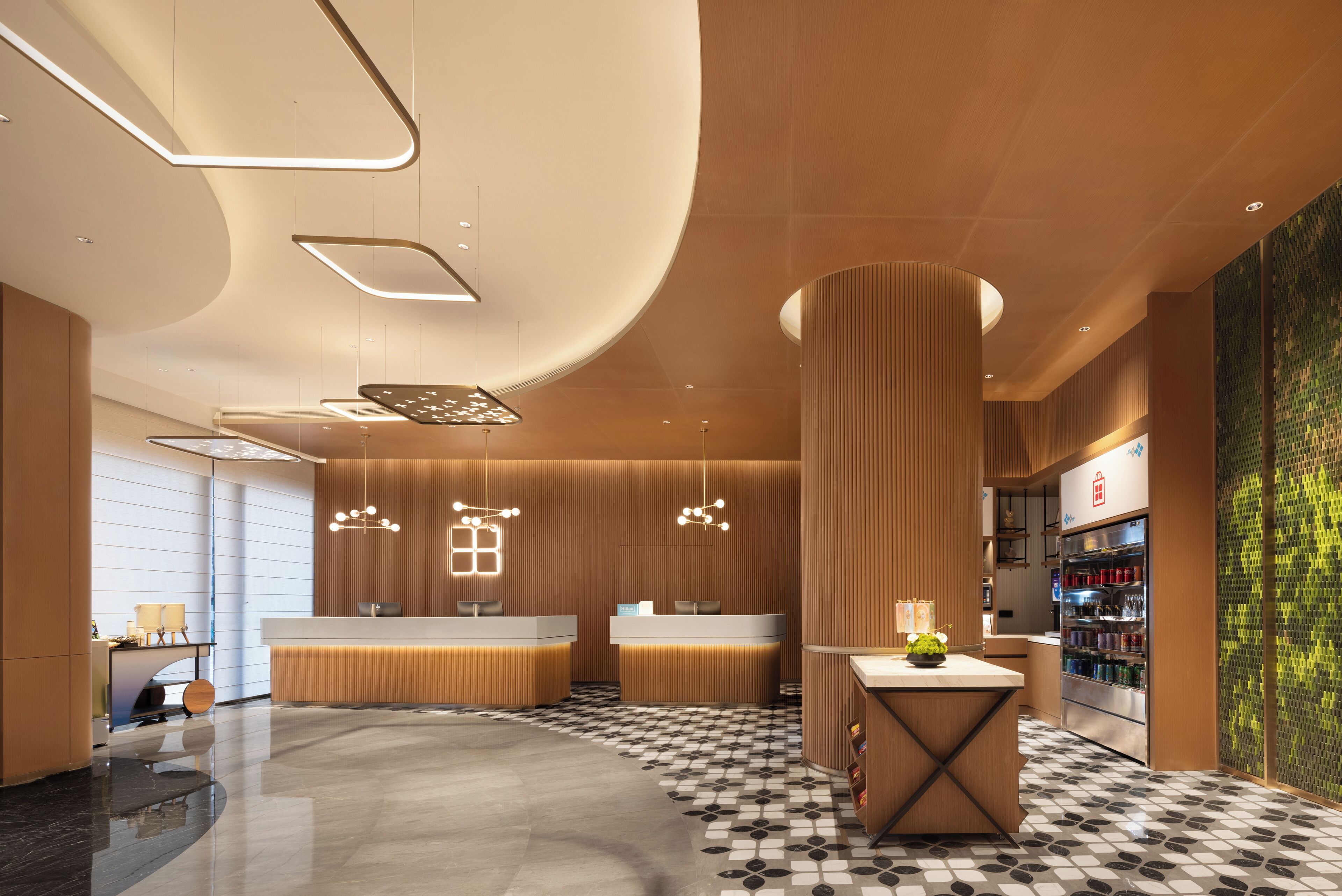 Eine moderne Hotellobby mit Empfangstresen, einem Café und einem Kühlschrank.