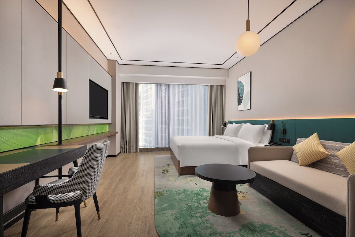 Ein Hotelzimmer mit Bett, Sofa, Esstisch, Stuhl, Fernseher und einem fenster mit Vorhängen.