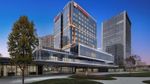 Un hôtel moderne avec une façade en verre, un logo bien visible sur le dessus et une galerie couverte à l’avant.