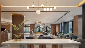 Un hall d’hôtel moderne avec une grande table à manger centrale, un coin salon et une grande plante en pot.