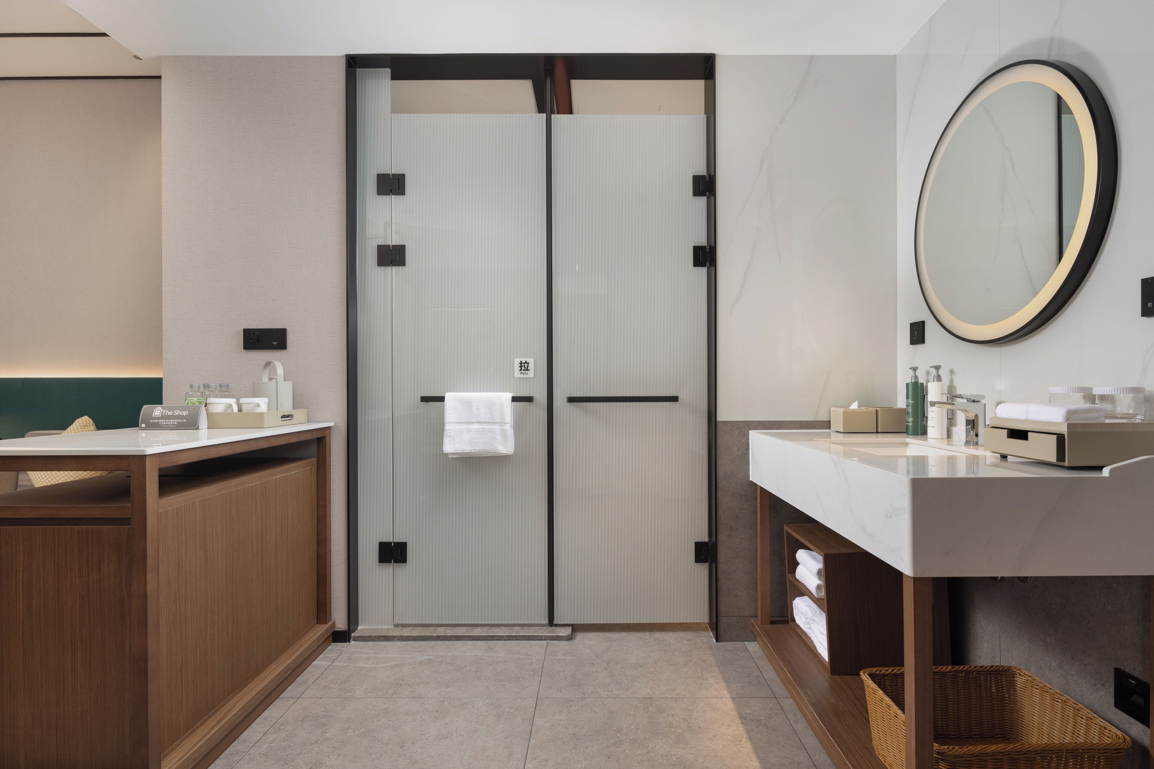 A modern bathroom with a double door, a large mirror, a wooden vanity, and a wicker basket.
