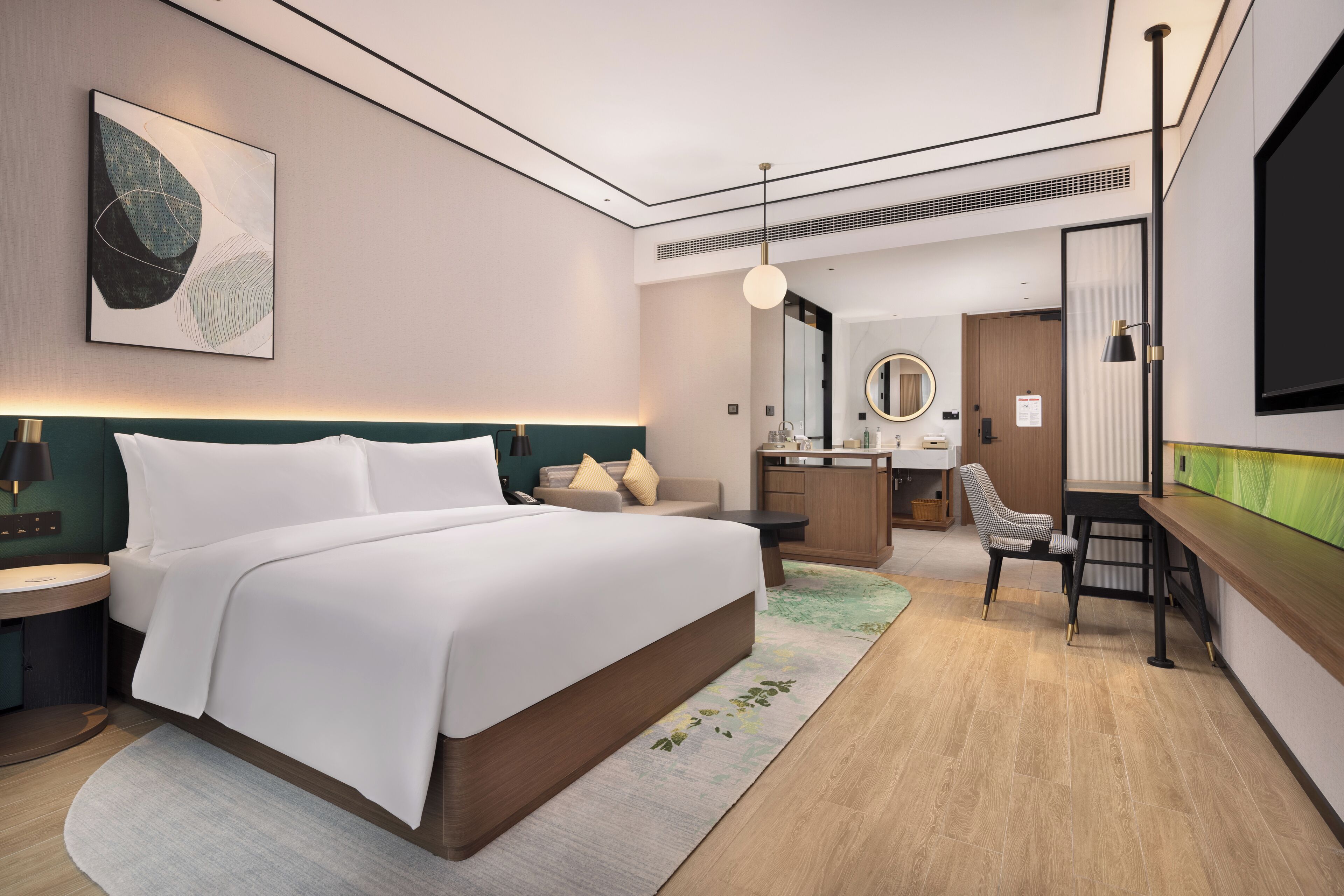 A modern hotel room with a large bed, a desk, a chair, a mirror, and a television.