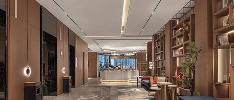 A modern hotel lobby with a central bar, seating areas, and a large window offering a city view.