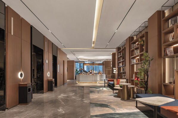 A modern hotel lobby with a central bar, seating areas, and a large window offering a city view.