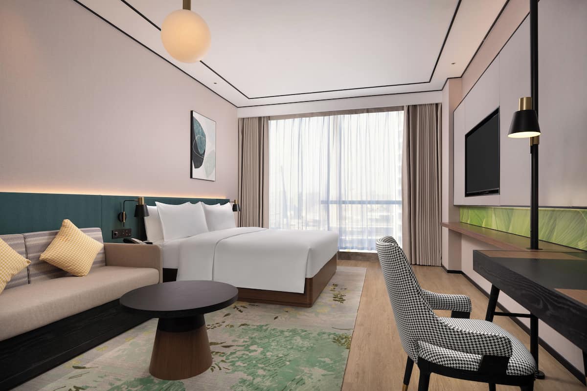 Ein modernes Hotelzimmer mit Bett, Sofa, Sessel und einem Flachbildfernseher.