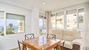 A modern room with a dining table, chairs, a sofa, and large windows offering a view of the sea and buildings. - Apartment 'Playa Algarrobo Costa' with Sea Views, Wi-Fi and Air Conditioning (Algarrobo-Costa)