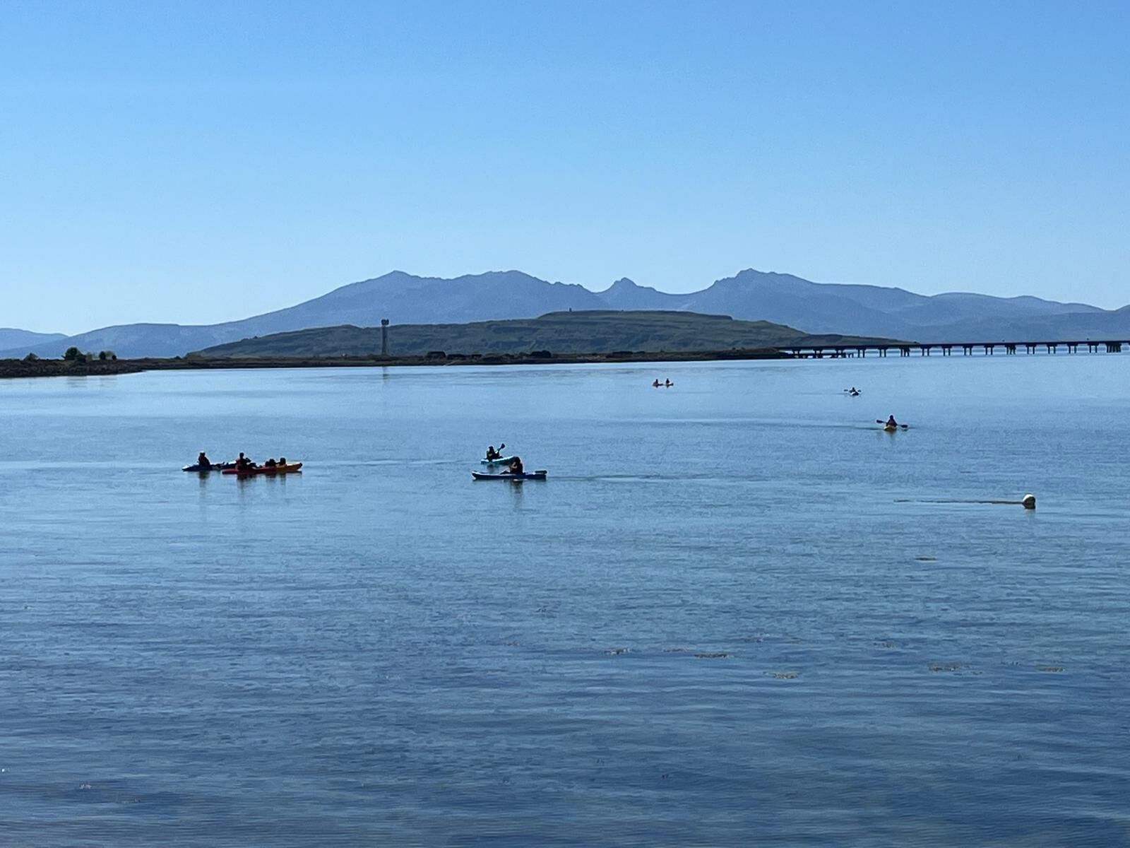 A calm lake with several kayaks and a long pier extending into the water.