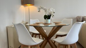 Un comedor moderno con una mesa de vidrio, sillas blancas, un jarrón de orquídeas blancas y una lámpara de pie.