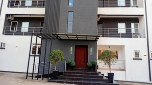 Ein modernes Gebäude mit roter Tür, zwei Kübelpflanzen und einer Uhr an der Fassade.