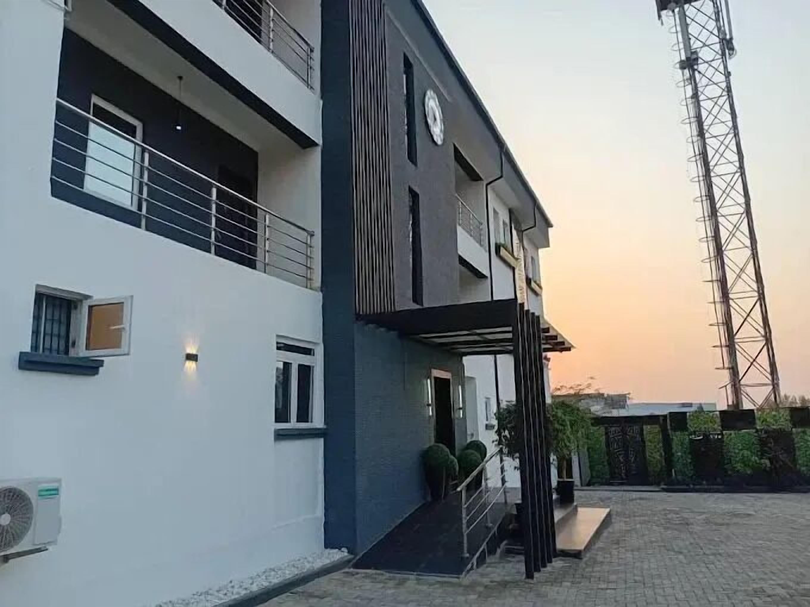 Un bâtiment moderne à deux étages, doté d’un balcon, d’un grand ventilateur et, au fond, d’un pylône de ligne électrique.
