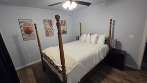 Una cama con dosel de madera y ropa de cama blanca, un ventilador de techo y obras de arte en las paredes.