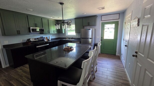 Una cocina moderna con gabinetes verdes, electrodomésticos de acero inoxidable, una isla grande con taburetes de bar y una puerta verde.