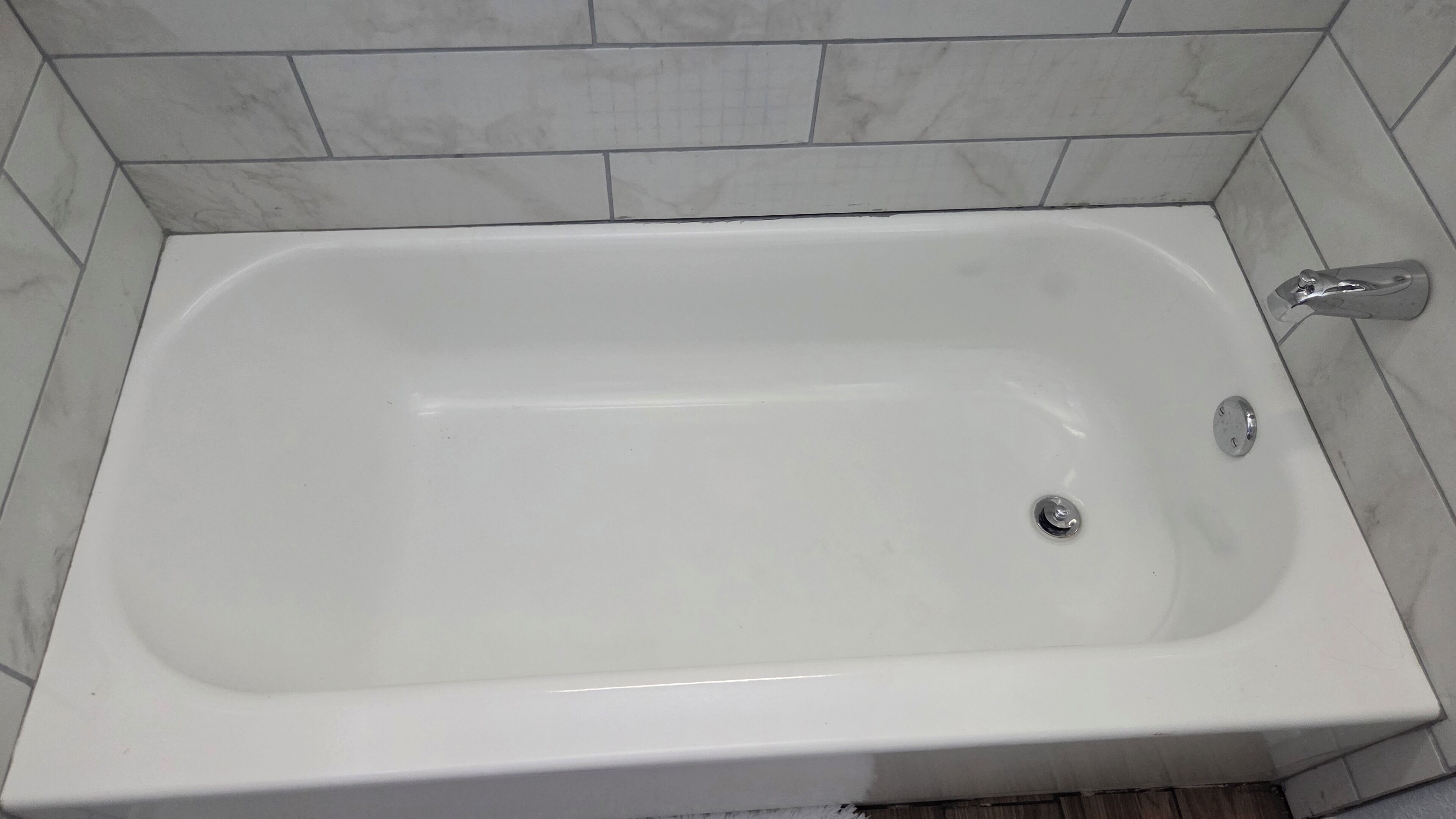 Une baignoire blanche, dotée d’un seul robinet et d’un drain, installée dans une salle de bain carrelée de marbre.