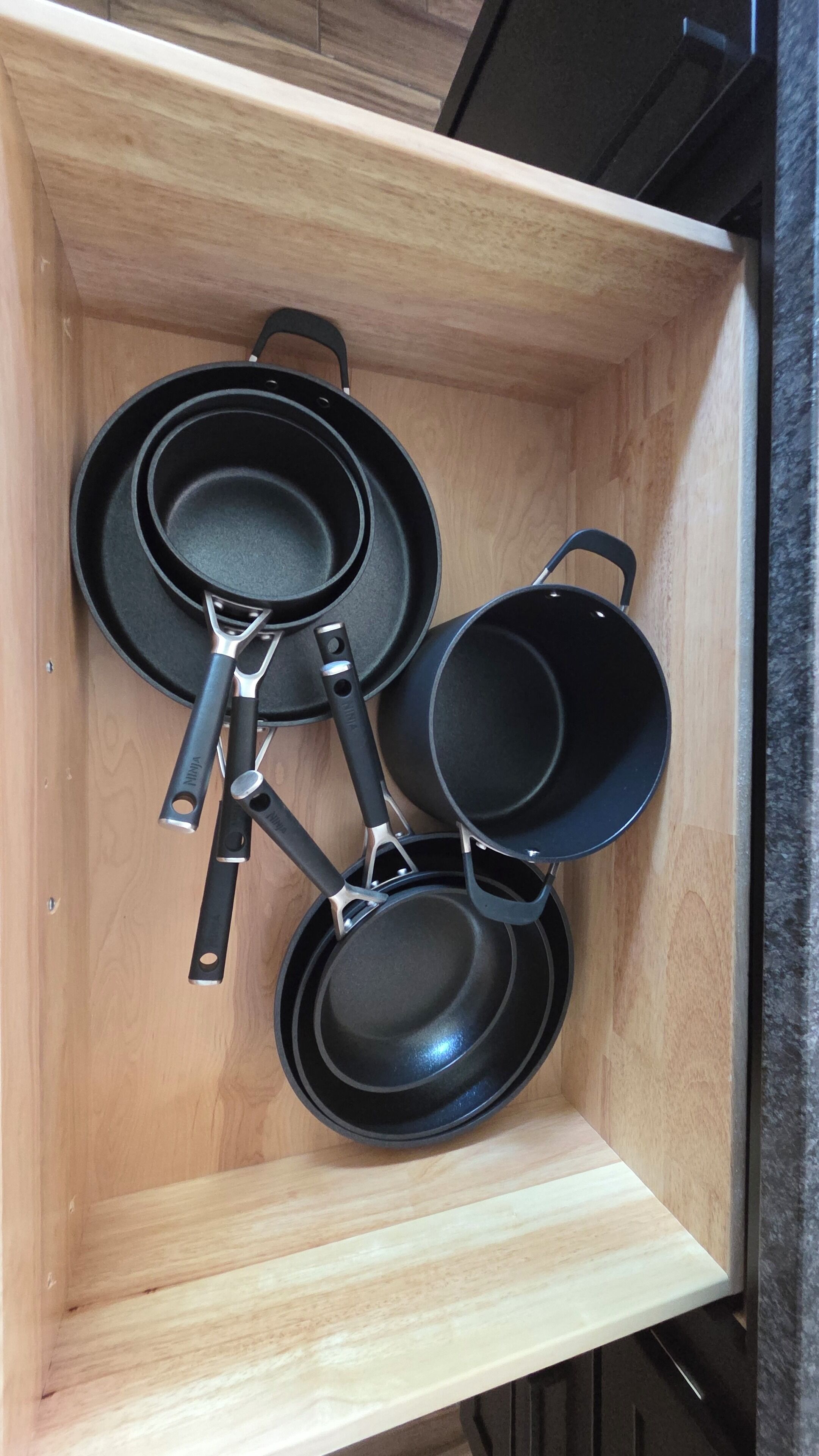 A kitchen drawer with three black frying pans and a pan holder.
