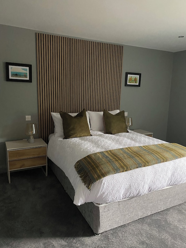 A neatly made bed with a white duvet and two green pillows, a bedside table with a lamp, and a striped throw blanket. - The Snug at the BH (Garrisker)