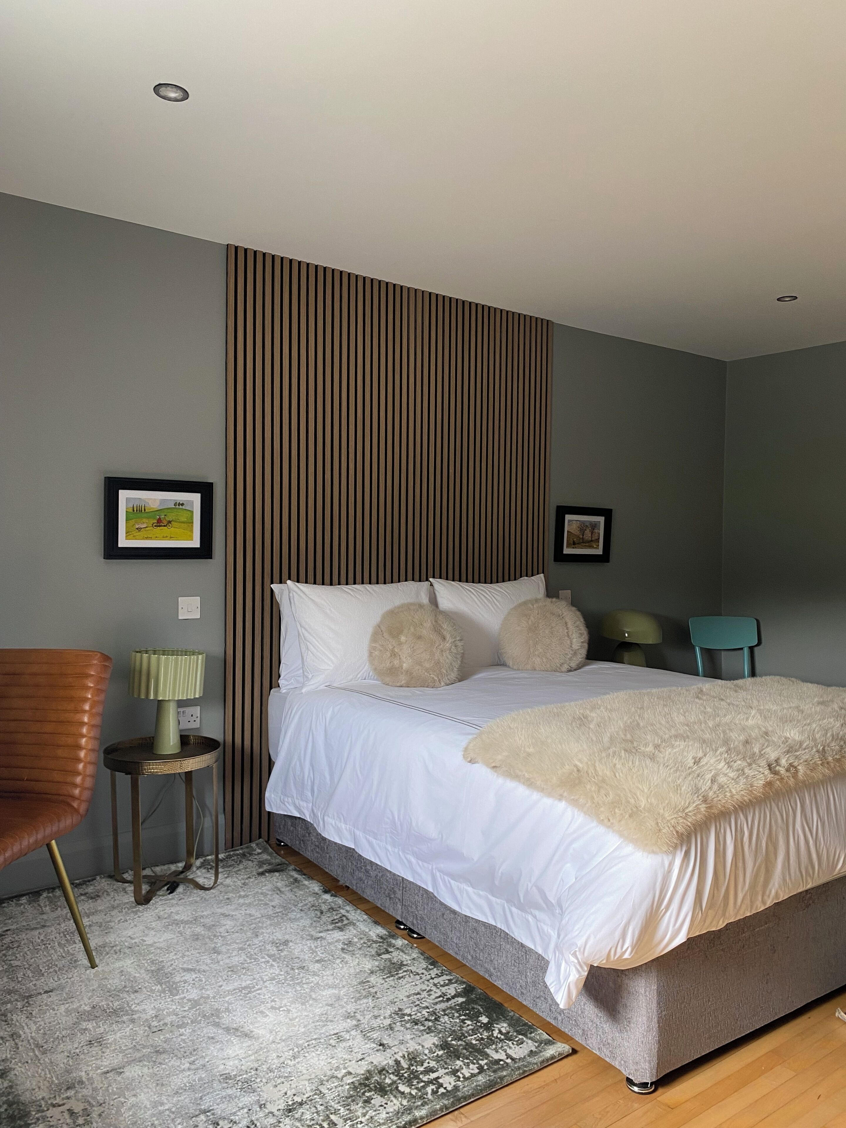 Een moderne slaapkamer met een groot bed, een nachtkastje met een lamp, een stoel en twee ingelijste foto's aan de muur.