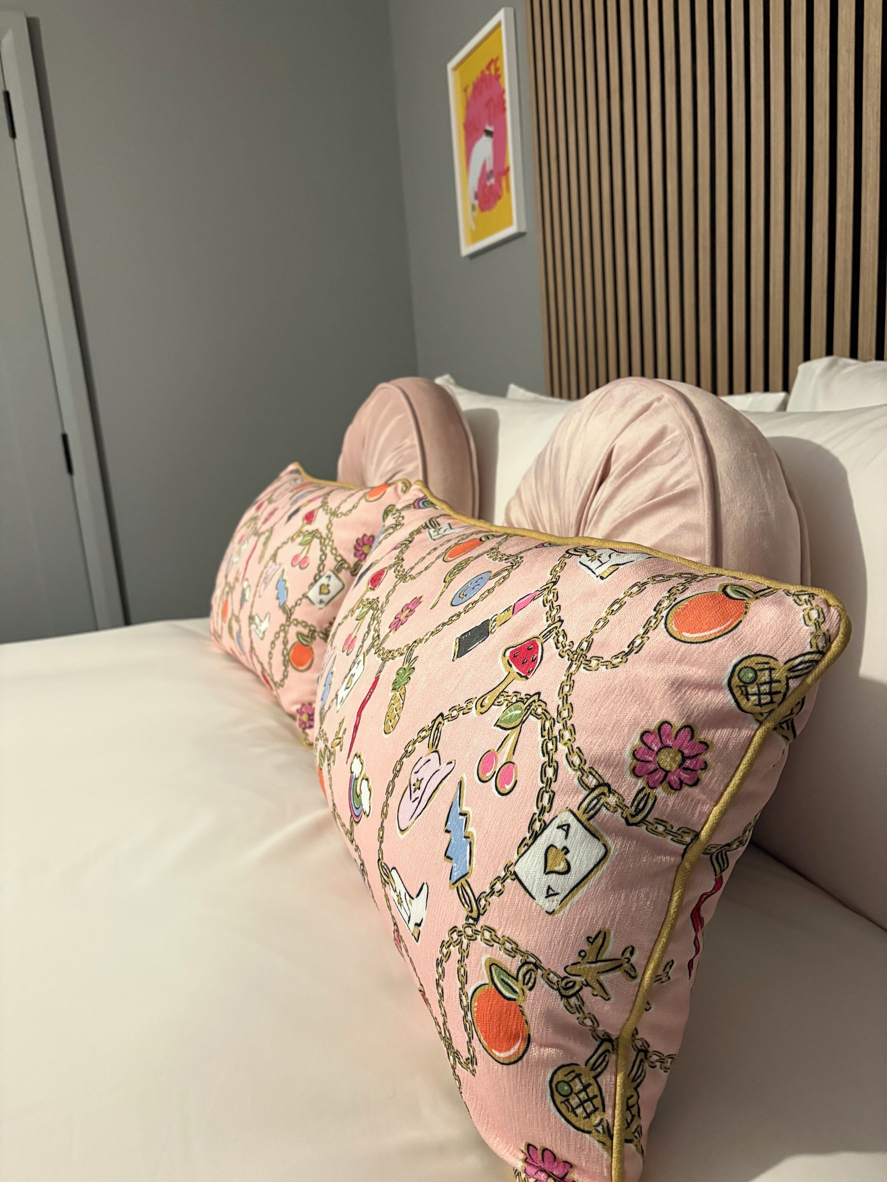 Een bed met een roze kussen met geborduurde motieven en een lijst met een afbeelding aan de muur.