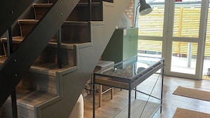 A staircase with a metal railing, a glass table with a metal frame, and a beige bag on the floor. - The Snug at the BH (Garrisker)