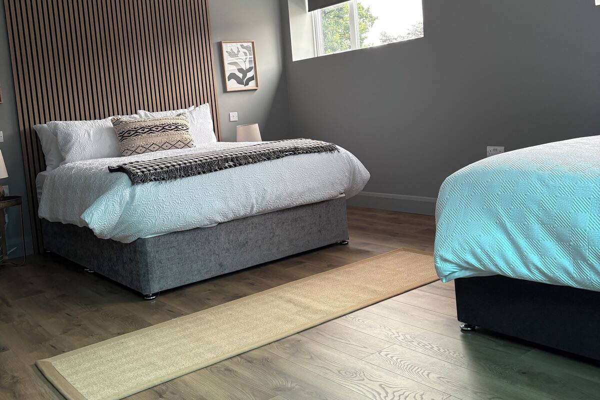 A modern bedroom with a large bed, a smaller bed, a window, and a wooden panel wall.