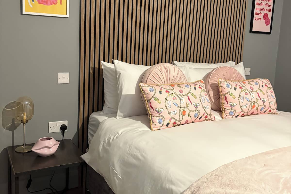 A bedroom with a bed, pillows, a bedside table with a lamp, and two wall art pieces.