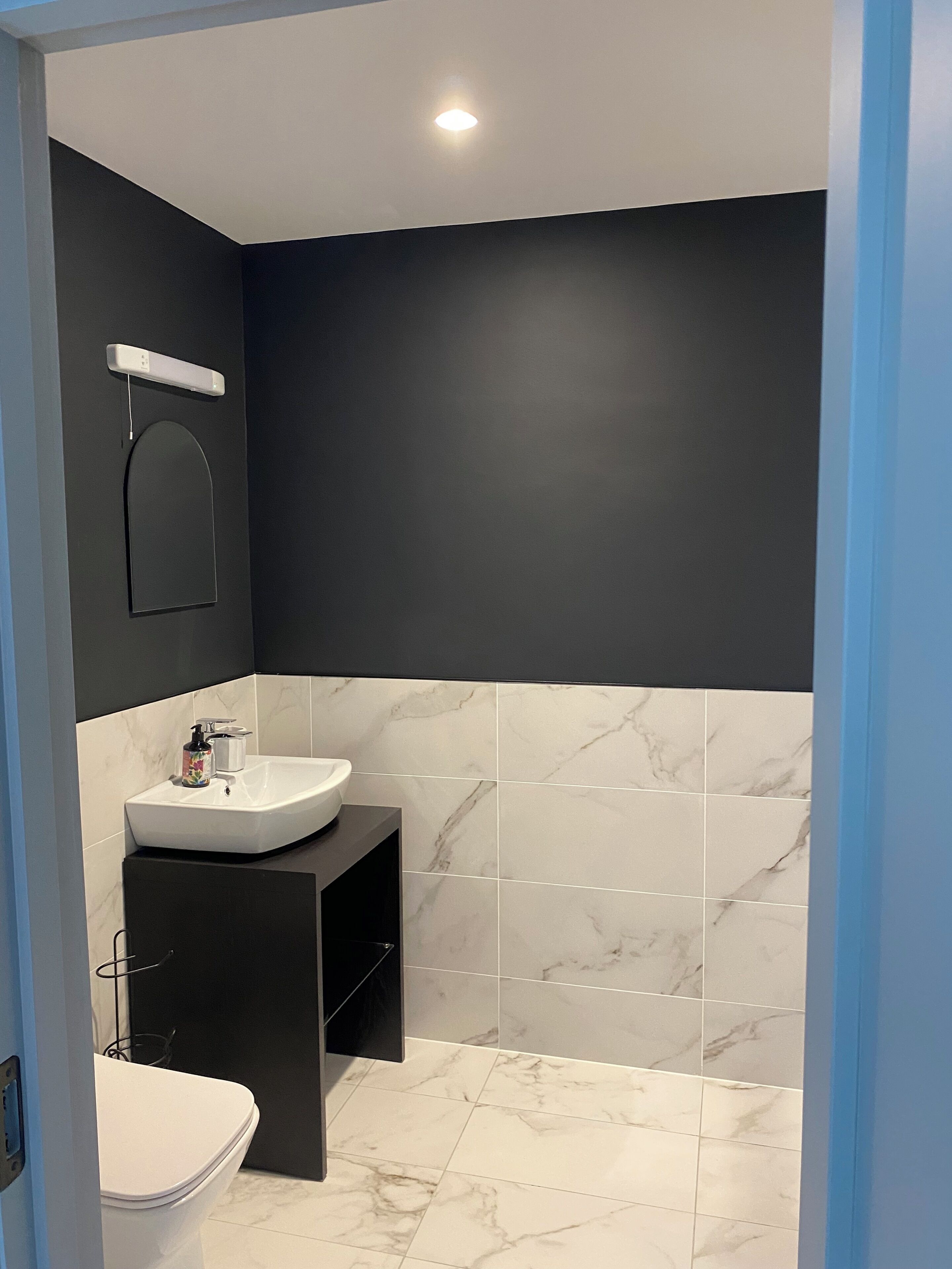 Un baño moderno con lavamanos blanco, tocador negro y un inodoro.