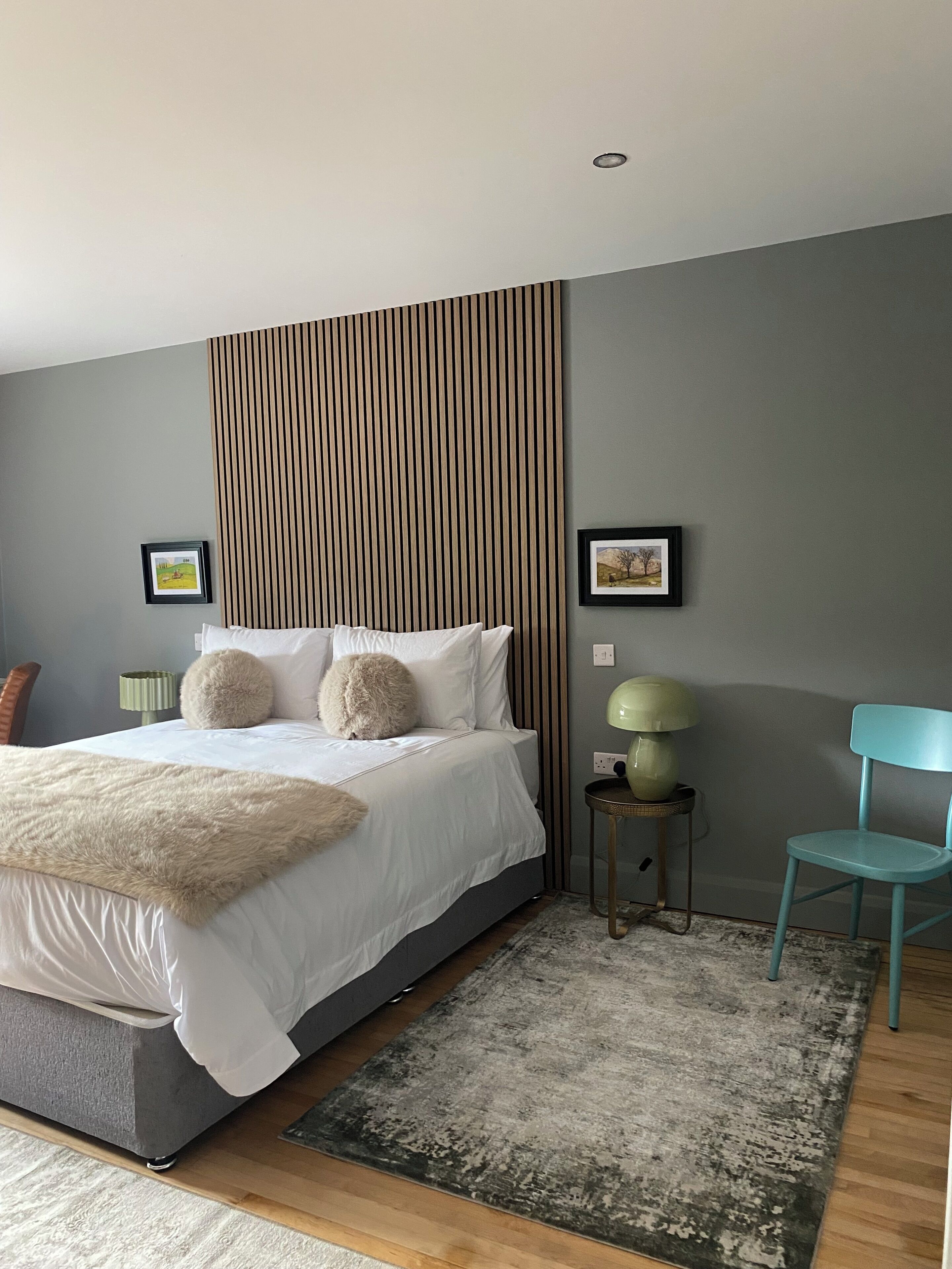 A modern bedroom with a large bed, a striped headboard, a small side table with a lamp, and a chair.