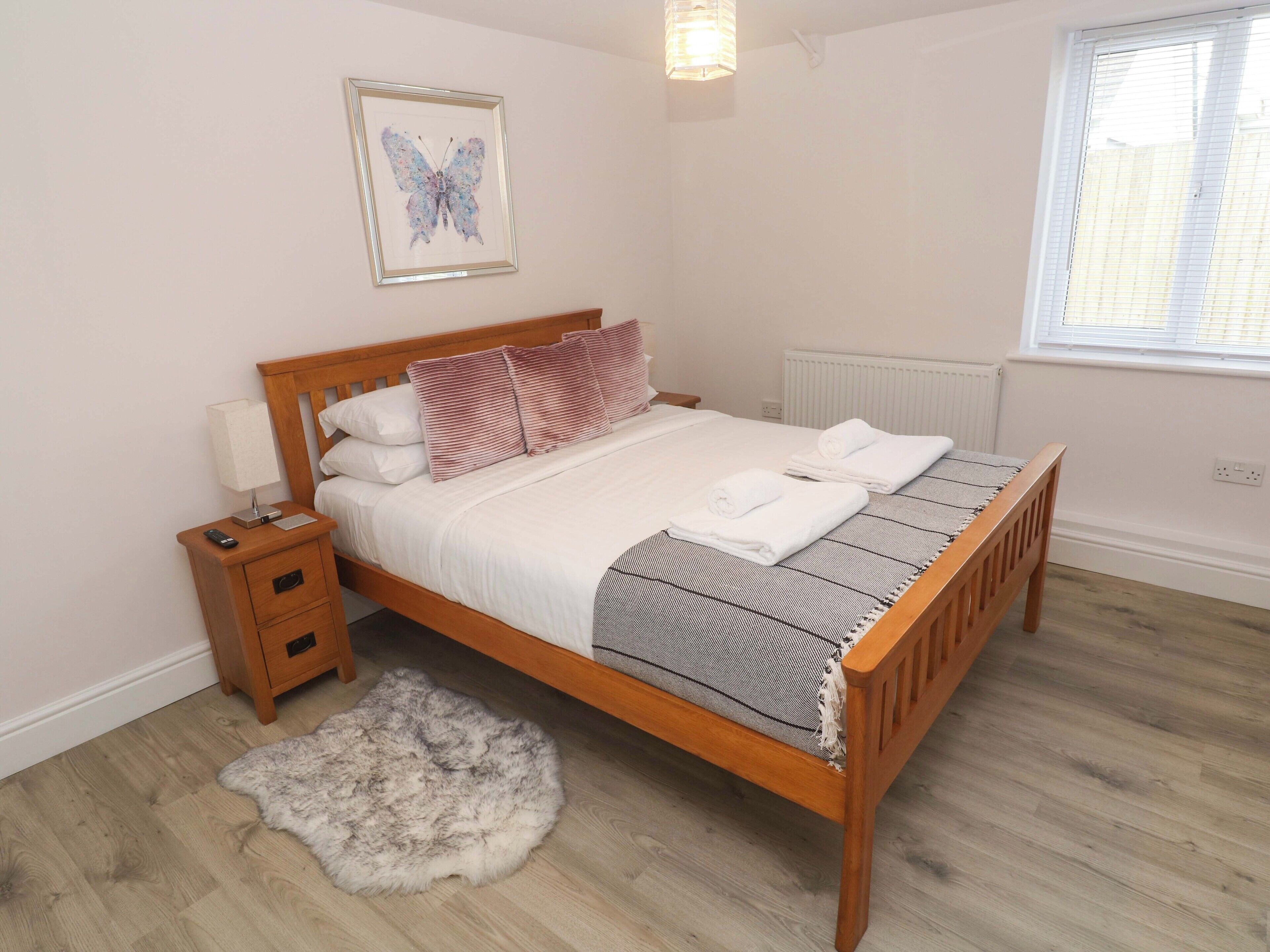 Una cama bien hecha con ropa blanca, una alfombra mullida y una mesita de noche con una lámpara.