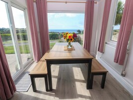 Una habitación con una mesa de madera y bancos, un florero con flores, y vistas al exterior a través de amplios ventanales.